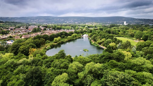 Cwmbran Boating Lake in Torfaen, Wales, surrounded by trees, with residential houses to one side.